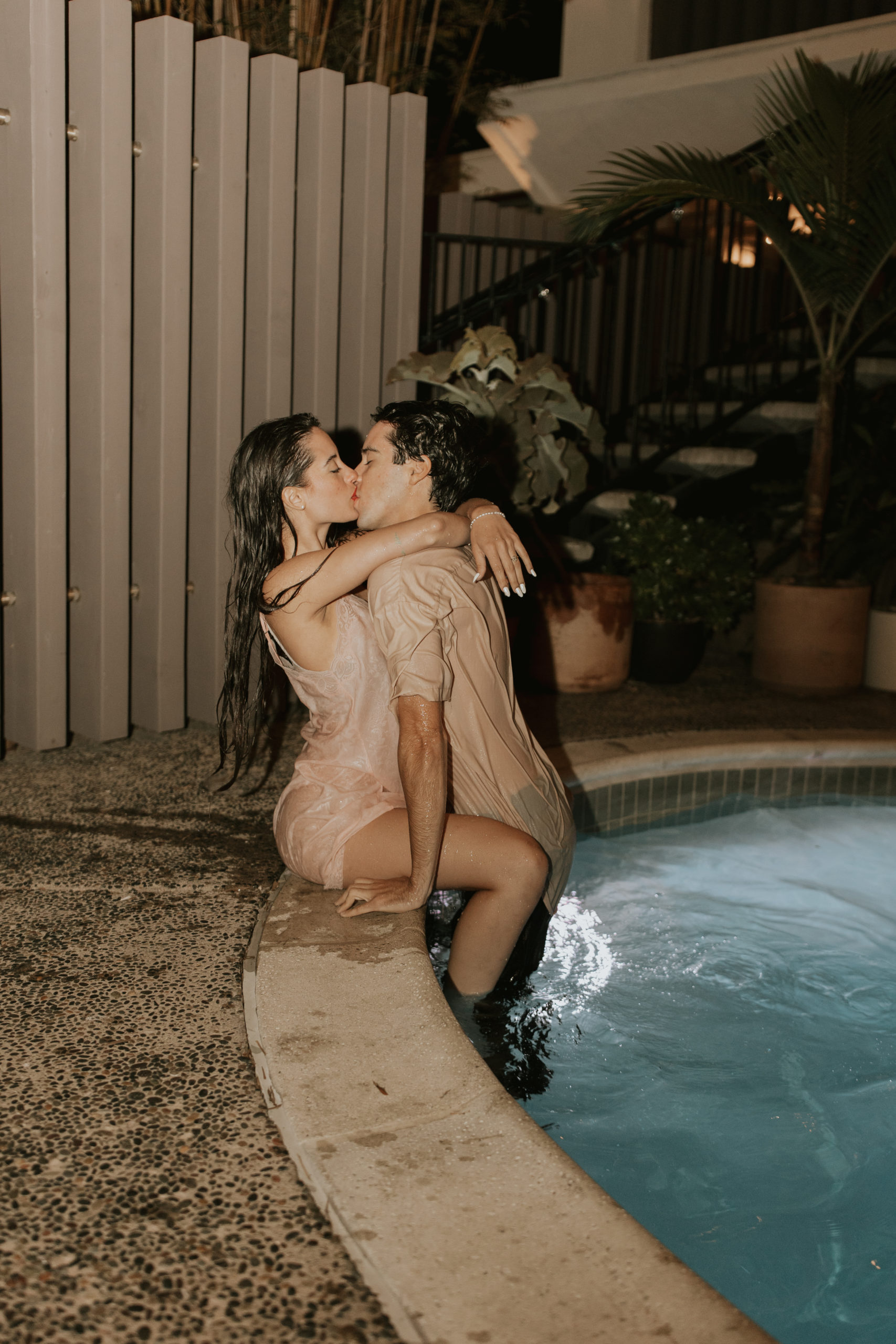 A couple kissing while sitting on the outside of a pool for an engagement session photoshoot in a boutique hotel