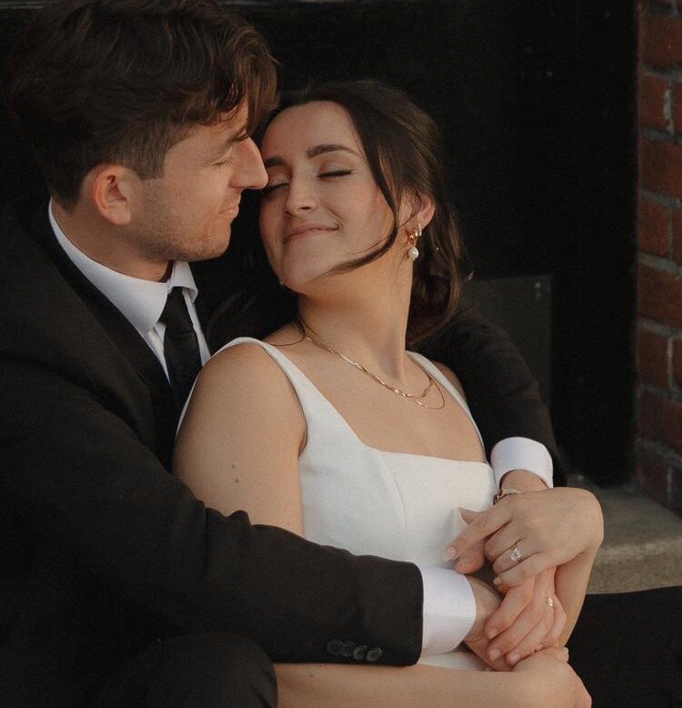 Bride and groom sitting in an urban setting and hugging while eyes are closed